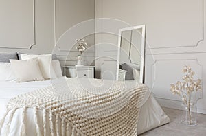 Beige woolen blanket on white bedding of king size bed in fashionable bedroom interior with grey wall