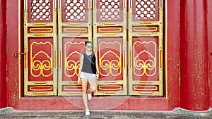 Beijing - A woman in shorts leaning against a massive red and golden doors inside of Forbidden City in Beijing, China