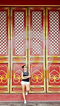 Beijing - A woman in shorts leaning against a massive red and golden doors inside of Forbidden City in Beijing, China