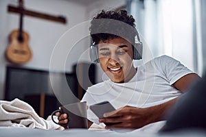 Being alone isnt bad at all. a young man using a smartphone and headphones while relaxing on his bed at home.