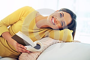 Being a bibliophile is the only positive addiction I know. a young woman reading a book while relaxing at home.