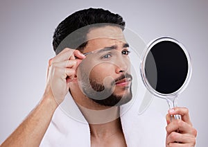 Being blessed with thick brows can be troublesome. a young man using a hand held mirror to tweeze his eyebrow.