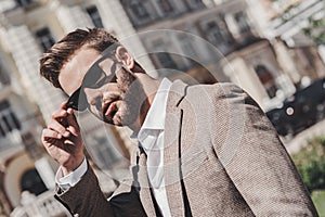 Being busy is a choice. Portrait of brown-haired man wearing sunglasses and looking at camera on the city streets.