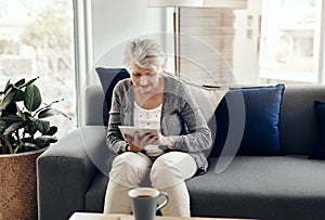 Being connected feels so good. a senior woman using a digital tablet while relaxing at home.