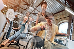 Being disabled does not mean you can`t be happy. Young positive asian man in wheelchair having fun with his colleagues