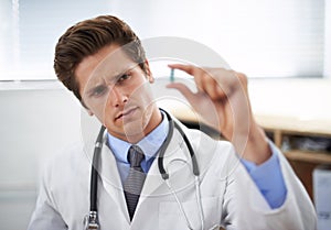 Being a healthy sceptic...a young doctor looking at pill he is holding.