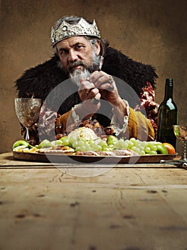 Being King has its perks. A mature king feasting alone in a banquet hall.