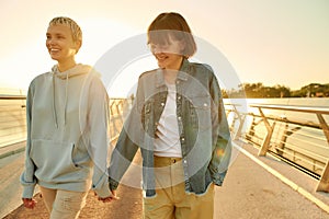 Being loved. Happy lesbian couple laughing, holding hands while walking on the bridge and watching the sunrise together