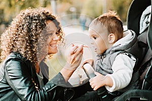 Being a mom concept - Portrait of mother feeding yogurt to 1 year old baby in stroller