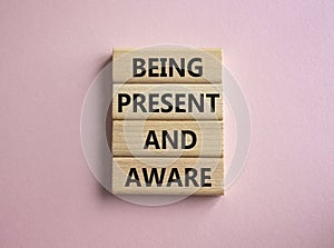 Being Present and Aware symbol. Wooden blocks with words Being Present and Aware. Doctor hand. Beautiful pink background.