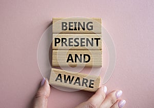 Being Present and Aware symbol. Wooden blocks with words Being Present and Aware. Doctor hand. Beautiful pink background.