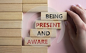 Being Present and Aware symbol. Wooden blocks with words Being Present and Aware. Doctor hand. Beautiful pink background.