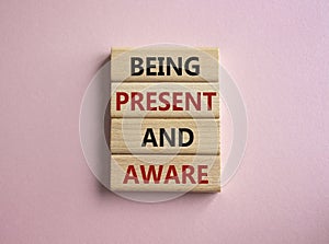 Being Present and Aware symbol. Wooden blocks with words Being Present and Aware. Doctor hand. Beautiful pink background.