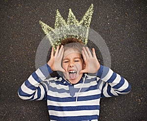 Being a silly billy. Top view shot of a young boy lying on the ground and pulling faces at the camera.