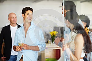 Being social with staff. A handsome young man with a glass of wine in his hand at an office social.