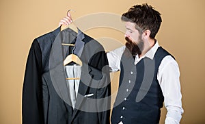 Being a tailor. Mens tailor. Hipster holding tailor made coats at department store. Bearded man choosing suit jacket in
