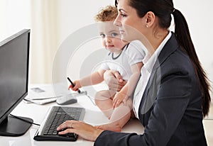 Being a working mom takes super powers. Working mother holding a baby while working on her computer.