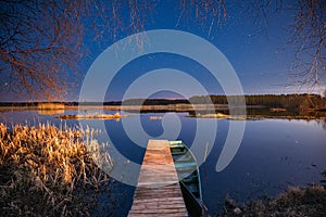 Belarus, Eastern Europe. Real Night Sky Stars Above Old Pier With Moored Wooden Fishing Boat. Natural Starry Sky And