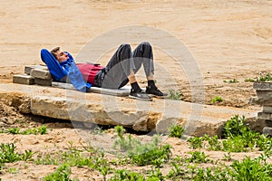 Belarus, Minsk - May 28, 2020: Young worker guy on a break resting, sleeping on an old concrete slab at a construction site