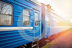 Belarusian passenger train waiting for passengers at the railway station with orange flares from evening sun