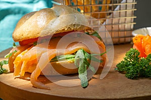 Belegtes BrÃÂ¶tchen mit RÃÂ¤ucherlachs, Rucola, Tomaten und Honig Senf Sauce auf einem Holzbrett mit Petersilie und einem kleinen photo