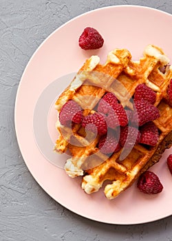 Belgian waffle with raspberries on pink plate over concrete background, top view. Close-up