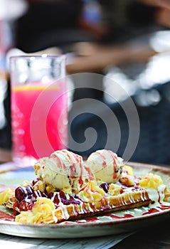 Belgian waffle with vanilla ice cream, strawberry sauce, custard and caramel on a plate on a restaurant table. Wholegrain flour