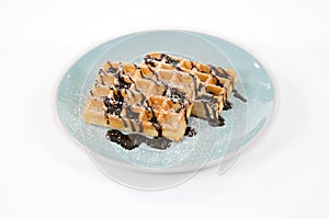 Belgian waffles with chocolate and powdered sugar on a blueish p