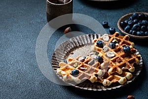 Belgian waffles with honey and fresh berries blueberry and hazelnut on dark background. Delicious dessert. Copy space