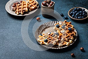 Belgian waffles with honey and fresh berries blueberry and hazelnut on dark background. Delicious dessert. Copy space