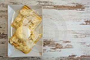 Belgian waffles with melted white chocolate, vanilla ice cream and coconut flakes on light wooden background.
