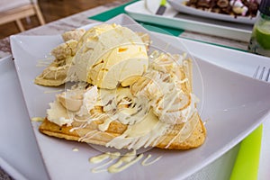 Belgian waffles with melted white chocolate, vanilla ice cream and coconut flakes on light wooden background.