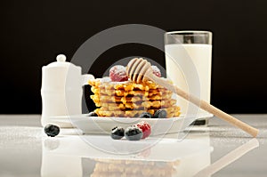 Belgian waffles with raspberries and sieving sugar powder and honey served with jug of milk on a white table