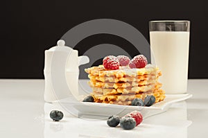 Belgian waffles with raspberries and sieving sugar powder and honey served with jug of milk on a white table