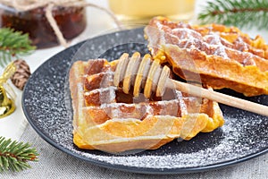 Belgian waffles sprinkled with icing sugar with a honey spoon on a black plate