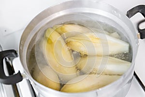 Belgian witloof vegetable is cooked in a saucepan on the stove.