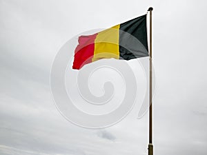 Belgium. National flag hoisted on the flagpole that flutters against the background of the cloudy and leaden sky
