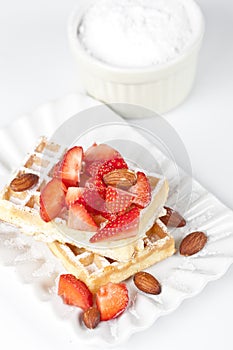 Belgium wafers with sugar powder, strawberries and almonds on ceramic plate on white table