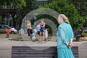 BELGRADE, SERBIA - AUGUST 2, 2015: Old woman looking at younger women taking care of children playing with balloons in the suburb