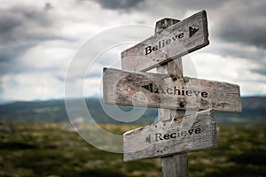 Believe, achieve and recieve text on wooden rustic signpost outdoors in nature/mountain scenery photo