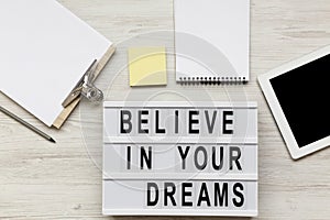 `Believe in your dreams` word on modern board, noticeboard, pencil and tablet over white wooden background, overhead view. Top v