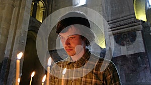 Believing man puts a candle and prays before an icon in the Orthodox Catholic Church