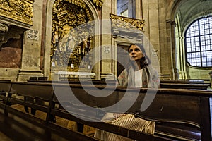 A believing woman sits on a bench in the church and prays to God. Girl praying in a church of Clerigos in Porto