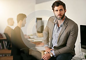 Believing in yourself is the first secret to success. Portrait of a young designer sitting on a desk with his colleagues