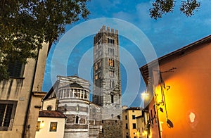 Bell tower of Chiesa di San Frediano catholic church and building with street lamp light on Piazza del Collegio square in historic