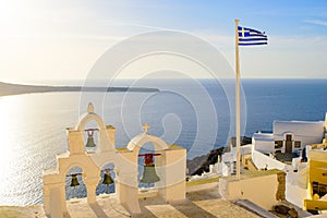 Bell tower and national flag of Greece in sunset light in Oia, Santorini, Greece