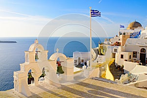 Bell tower and national flag of Greece in sunset light in Oia, Santorini, Greece