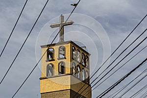 Bell tower with symmetrically arched windows with a cross on top with a blue sky