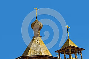 The bell tower of a wooden Orthodox Christian church. Crosses on the main dome and on the roof of the bell tower.