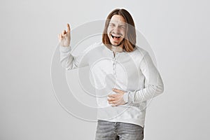 Belly aches from laughing out loud. Portrait of pleased happy handsome guy with beard and long fair hair pointing up or